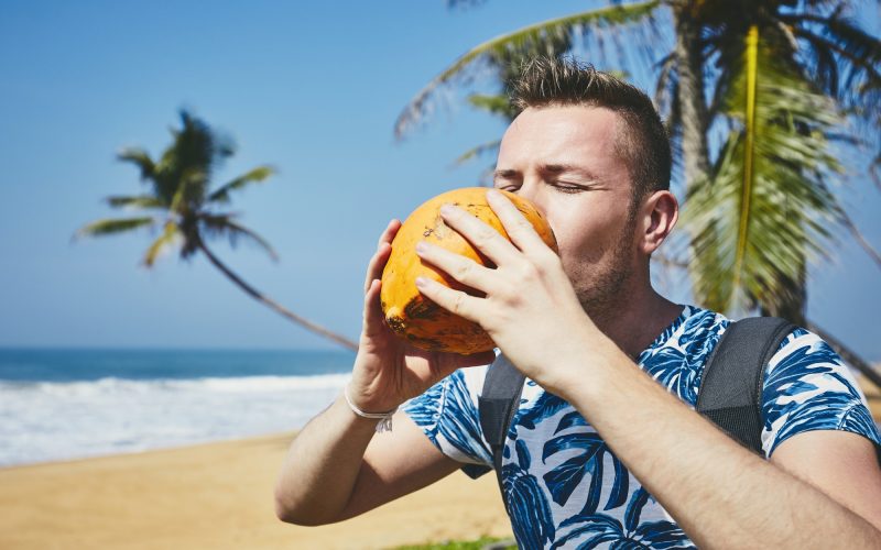 Thirsty young man drinking coconut water. Relaxation on the sand beach. Sri Lanka